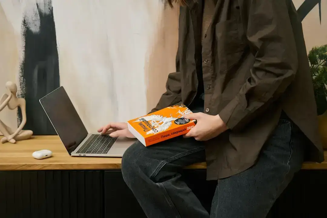 Person holding book beside laptop